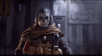 A Soldier With A Skull On His Head Is Standing In Front Of A Wall With Arabic Writing GIF