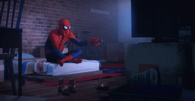 A Spider Man Is Sitting On A Bed Holding A Remote Control GIF