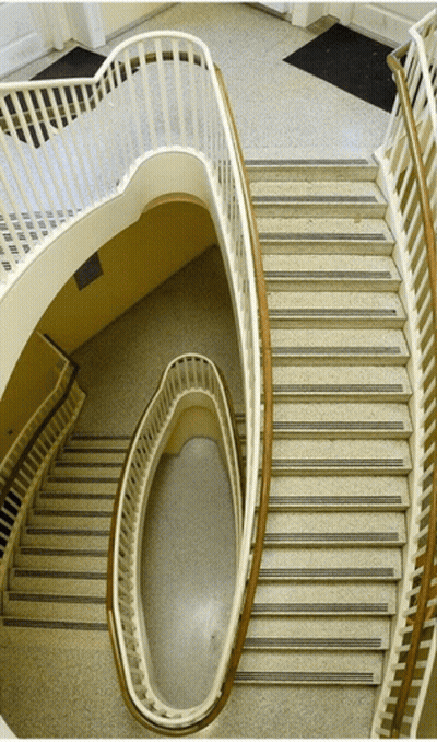 A Spiral Staircase With A White Railing And A Black Mat On The Ground GIF