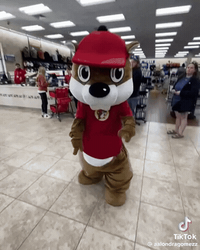 A Squirrel Mascot Is Standing In A Store With A Red Hat On GIF