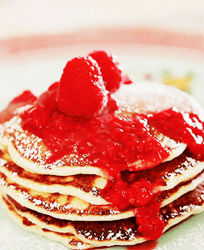 A Stack Of Pancakes Topped With Raspberries And Powdered Sugar GIF