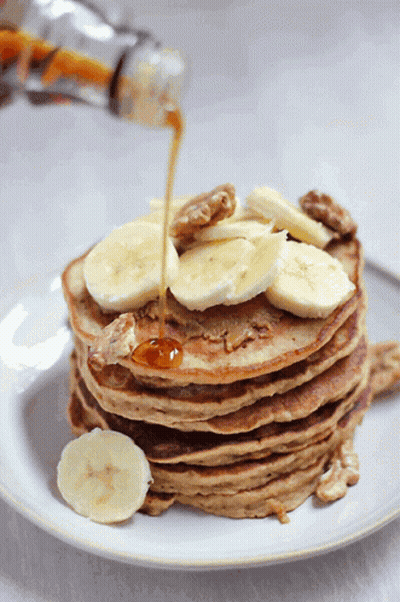 A Stack Of Pancakes With Bananas And Walnuts Being Poured Syrup On Top GIF