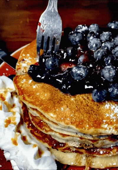 A Stack Of Pancakes With Blueberries On Top And Whipped Cream On The Side GIF