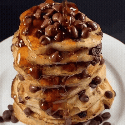 a stack of pancakes with chocolate chips on top on a white plate .