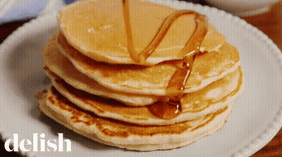 A Stack Of Pancakes With Syrup Being Poured On Them Is On A White Plate With The Word Delish On It GIF