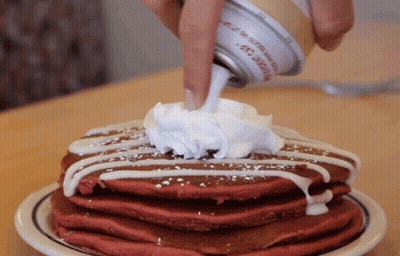 A Stack Of Red Velvet Pancakes With Whipped Cream Being Poured On Top GIF
