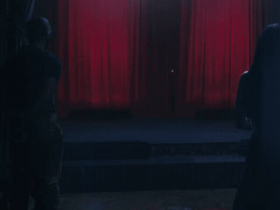 A Stage With A Red Curtain And A Few People Watching GIF