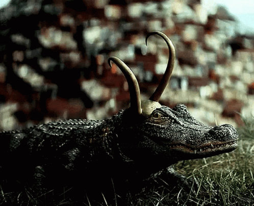 A Statue Of A Crocodile With Horns Is Laying In The Grass GIF