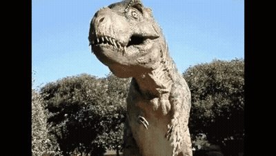 A Statue Of A Dinosaur Is Standing In Front Of Some Trees GIF