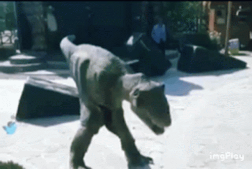 A Statue Of A Dinosaur Is Walking On A Beach . GIF
