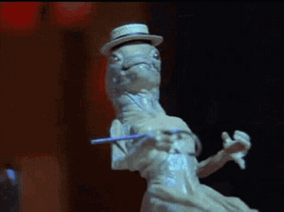 A Statue Of A Lizard Wearing A Hat And Holding A Cane Is Dancing . GIF