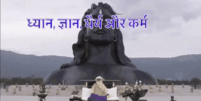 A Statue Of A Man Sitting In Front Of A Large Statue Of A Man GIF
