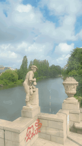 A Statue Of A Man Standing Next To A Body Of Water With Graffiti On The Wall That Says ' Shaolia ' GIF