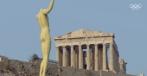 A Statue Of A Naked Man Stands In Front Of A Building With The Olympic Rings On The Bottom GIF