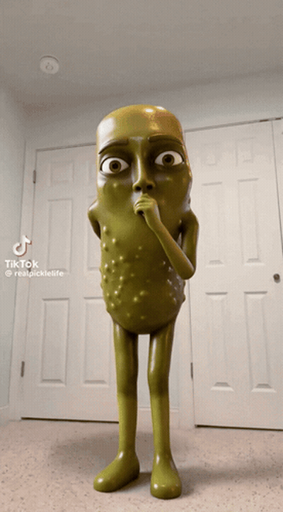 A Statue Of A Pickle With A Surprised Look On His Face Is Standing In Front Of A Door GIF
