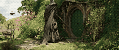 A Statue Of A Wizard Standing In Front Of A Hobbit House GIF