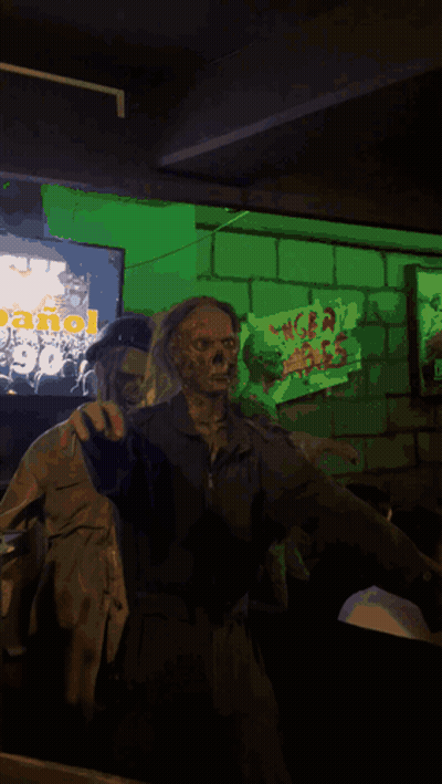 A Statue Of A Zombie Wearing A Goggles And Holding A Yellow Sign With A Hand On It GIF