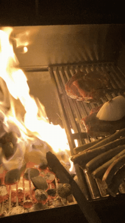 A Steak Is Being Cooked On A Grill With Flames Behind It GIF