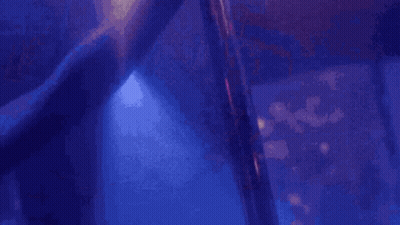 A Stripper Is Dancing On A Pole In A Dark Room With Purple Lights . GIF