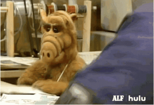 A Stuffed Animal From The Show Alf Is Sitting At A Desk Talking On A Cell Phone GIF