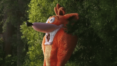 A Stuffed Animal In A Crash Bandicoot Costume Peeking Out From Behind Some Trees GIF