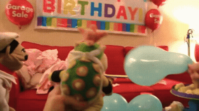 A Stuffed Animal Is Blowing Up A Blue Balloon In Front Of A Birthday Banner GIF