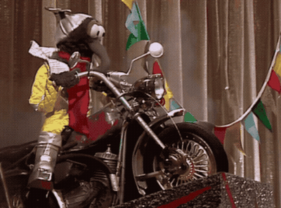 A Stuffed Animal Is Riding A Motorcycle With Flags Behind It GIF
