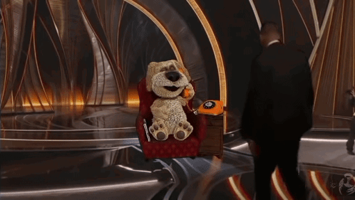 A Stuffed Animal Is Sitting In A Chair Talking On A Telephone GIF