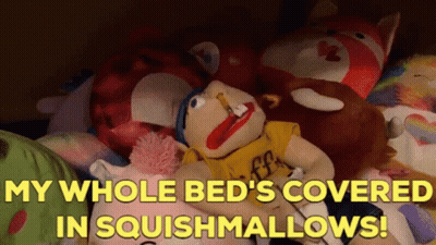 A Stuffed Animal Laying On A Bed With The Words " My Whole Bed 'S Covered In Squishmallows ! " GIF