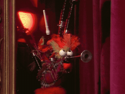 A Stuffed Animal With Big Eyes Is Holding A Bagpipe In Front Of A Red Curtain GIF