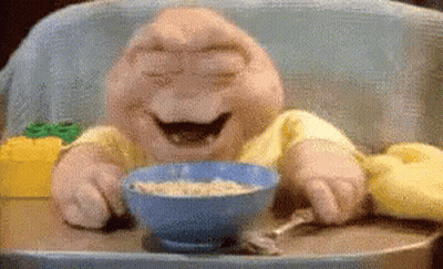 A Stuffed Baby Is Sitting In A High Chair Eating Cereal GIF