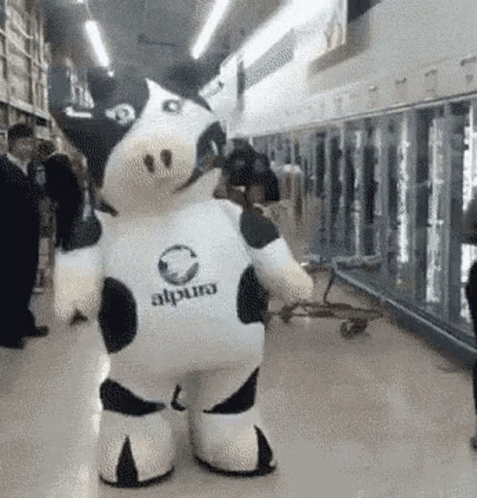 A Stuffed Cow Mascot Is Standing In A Supermarket . GIF