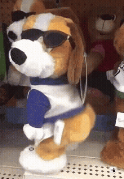 A Stuffed Dog Wearing Sunglasses And A Blue Shirt Is Standing On A Shelf GIF