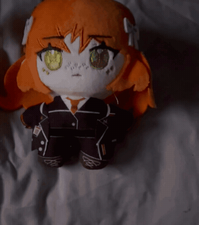 A Stuffed Doll With Orange Hair And Yellow Eyes Is Laying On A White Sheet GIF