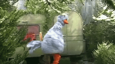 A Stuffed Duck Is Standing In Front Of A Trailer In A Forest . GIF