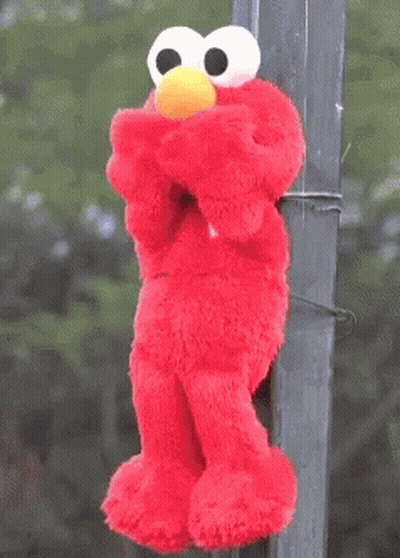A Stuffed Elmo With A Yellow Hat Is Hanging On A Pole GIF