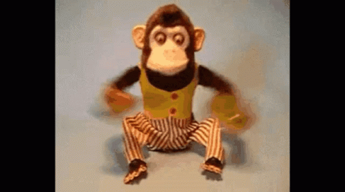 A Stuffed Monkey In Striped Pants Is Sitting On A Blue Surface . GIF