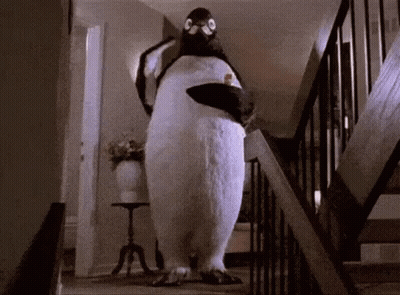 A Stuffed Penguin Is Walking Down A Set Of Stairs In A House . GIF