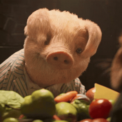 A Stuffed Pig Wearing A Striped Shirt Is Sitting In Front Of A Bowl Of Fruits And Vegetables GIF
