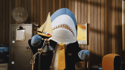 A Stuffed Shark In A Suit And Tie Holds A Small Boat GIF