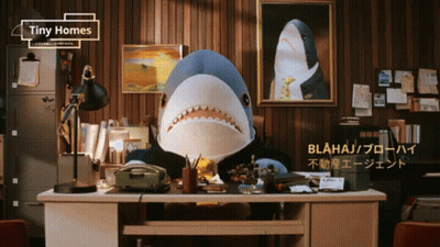 A Stuffed Shark Is Sitting At A Desk With Tiny Homes Written On The Top GIF