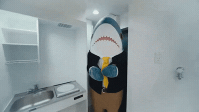 A Stuffed Shark Is Standing In A Kitchen Wearing A Suit And Tie GIF