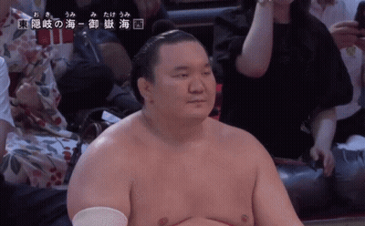 A Sumo Wrestler Is Sitting In A Stadium With Chinese Writing On The Bottom Right GIF