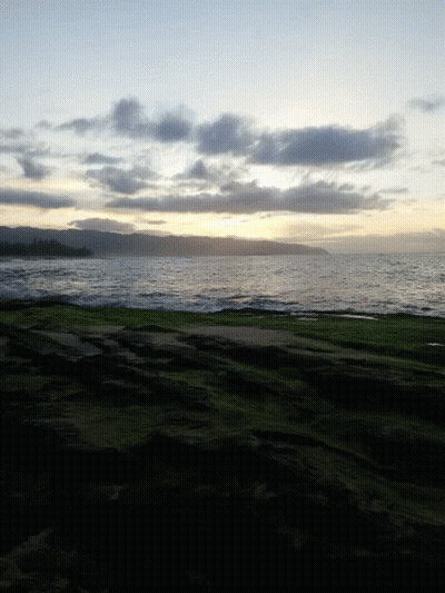 A Sunset Over A Body Of Water With A Grassy Hill In The Foreground GIF
