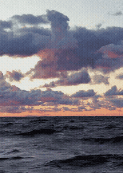A Sunset Over A Large Body Of Water With Clouds GIF