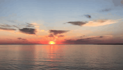 A Sunset Over A Large Body Of Water With The Sun Shining Through The Clouds GIF