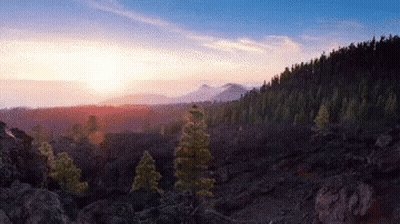 A Sunset Over A Valley With Trees And Rocks In The Foreground GIF