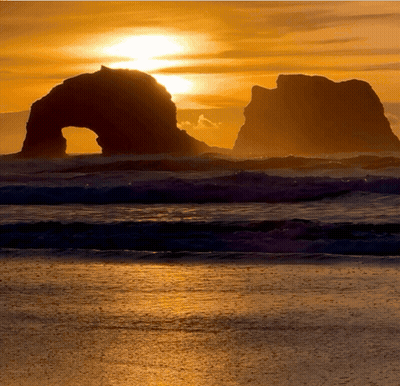 A Sunset Over The Ocean With A Large Rock Formation In The Foreground GIF