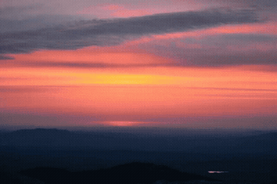 A Sunset With Mountains In The Foreground And A Dark Sky In The Background GIF