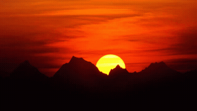 A Sunset With Mountains In The Foreground And A Large Sun In The Background GIF